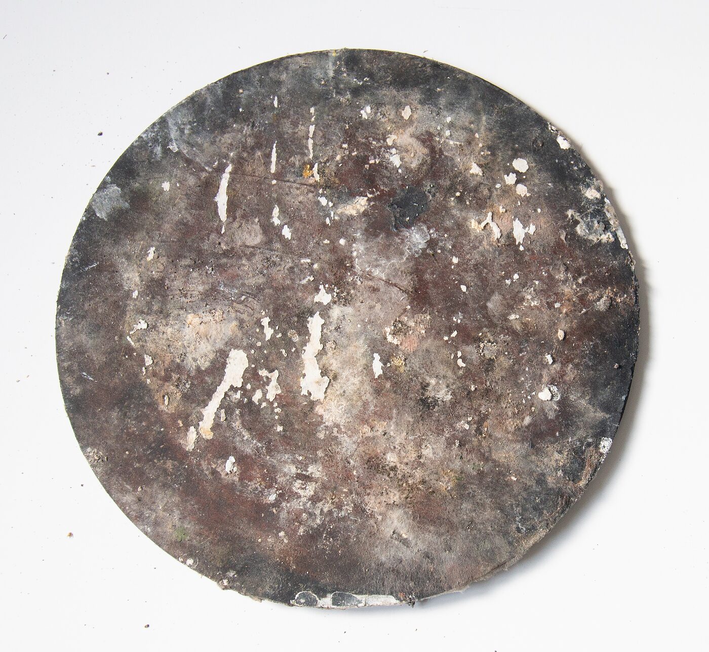 Circular masonite tondo. Charred greys and browns across the disc with scattered chalky white spalling, pitted texture reading as cratered planetary surface.