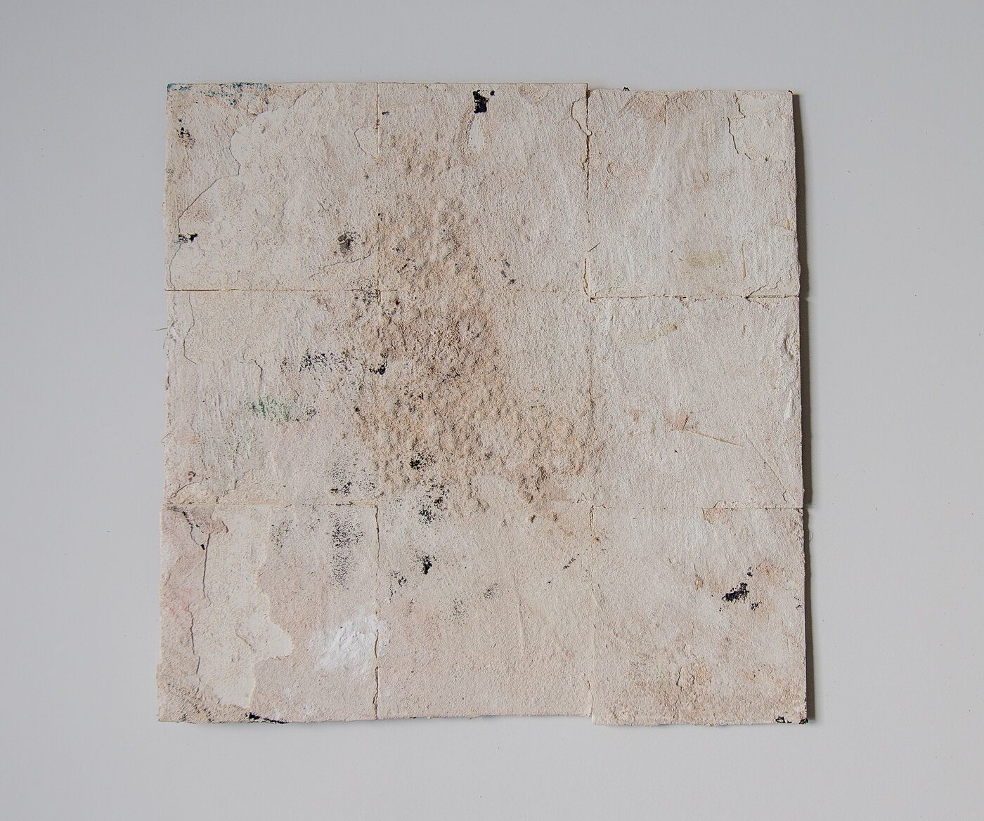 Square masonite. Pale cream and bone-white surface across the whole tile with subtle pink and grey blooms, traces of black mark-making near the upper edge, folded and creased texture.